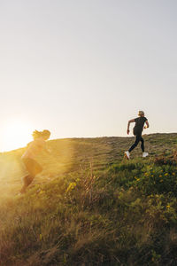 Women running up on hill against sky on sunset