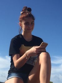 Low angle view of young woman using smart phone against sky