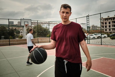Young adult caucasian man plays basketball at outdoor sports court in the evening