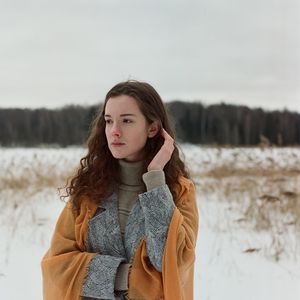 A woman stands on the shore of a frozen lake in a yellow scarf