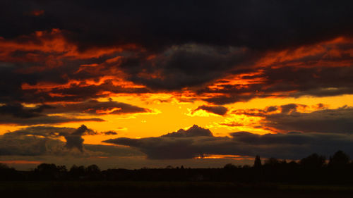 Scenic view of dramatic sky over silhouette landscape during sunset