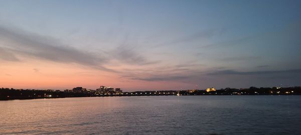 Sea by illuminated buildings against sky during sunset