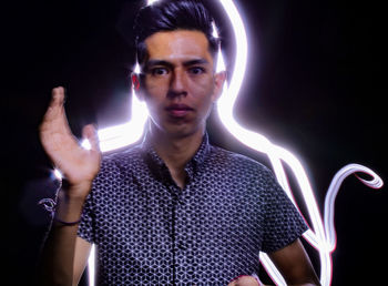 Portrait of young man standing against black background