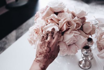 Cropped henna tattooed hand of bride touching rose bouquet