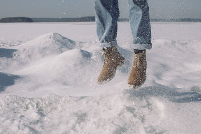 Low section of person jumping on snow covered land