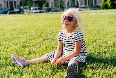Happy smiling little girl sits on a lawn in an urban environment. 