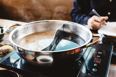 Midsection of person sitting by kitchen utensil on table