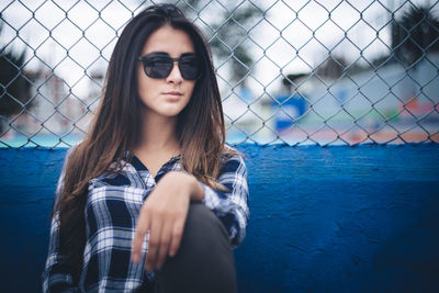 Portrait of beautiful young woman wearing sunglasses by fence