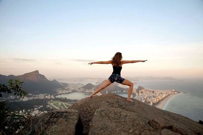 Woman exercising on rock by sea against clear sky