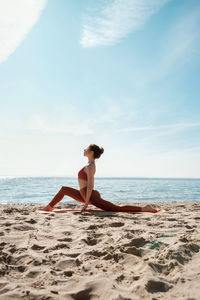 Full length of woman exercising on beach against sky