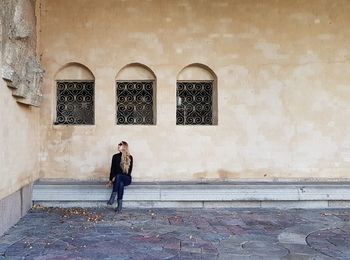 Full length of woman sitting on seat against building