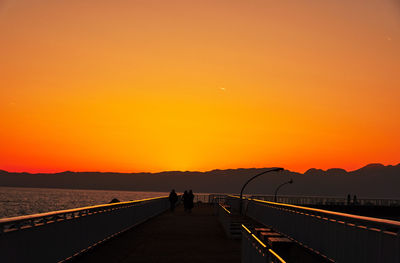 Silhouette people on sea against orange sky during sunset