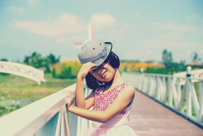 Young woman wearing hat standing against railing