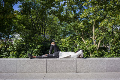 Man with cap on face lying on retaining wall at park