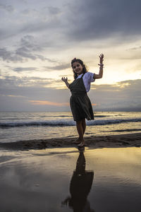 Low angle view portrait of girl standing at beach against sky during sunset