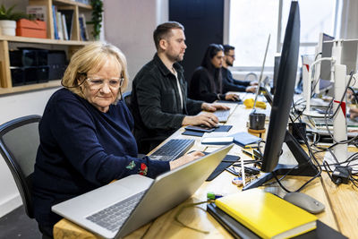 Senior businesswoman working on laptop with colleagues at desk