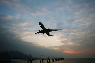 Low angle view of silhouette airplane flying over sea against sky during sunset