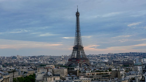 Tower amidst buildings in city against cloudy sky