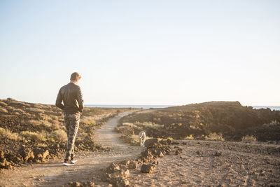 Rear view of man walking on land against clear sky