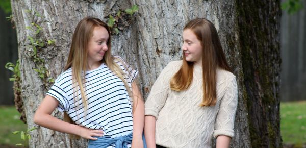 Happy friends looking each other against tree trunk at public park