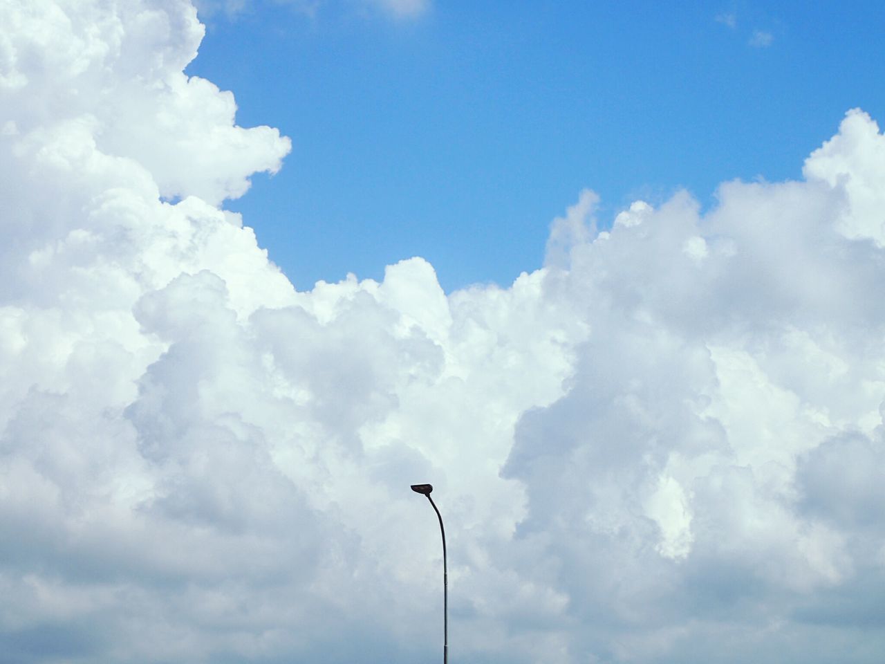 low angle view, sky, cloud - sky, cloud, cloudy, blue, street light, nature, tranquility, beauty in nature, day, outdoors, lighting equipment, scenics, pole, white color, cloudscape, no people, tranquil scene, high section