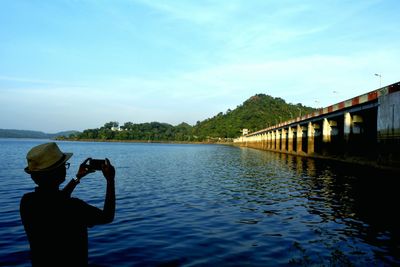 Silhouette man photographing masanjor dam through mobile phone