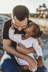 Young girl sitting in father’s lap giving a kiss at beach