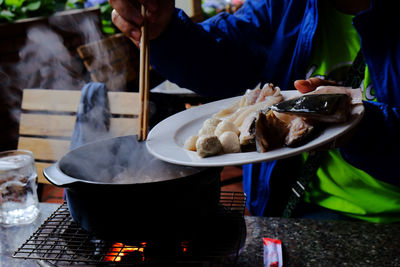 Scraping fish parts into a cooking pot with chopsticks.