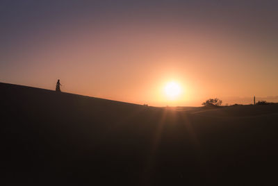Silhouette man standing on sand dune against clear sky during sunset