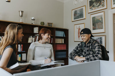 Happy male and female students talking against bookshelf in library