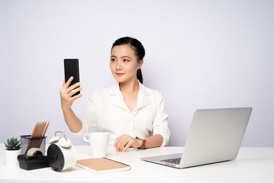 Mid adult woman using laptop on table against white background