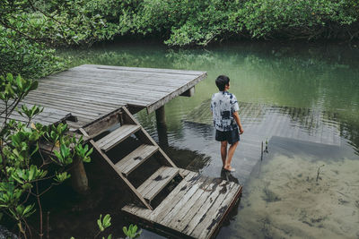 Rear view of boy standing by lake against trees