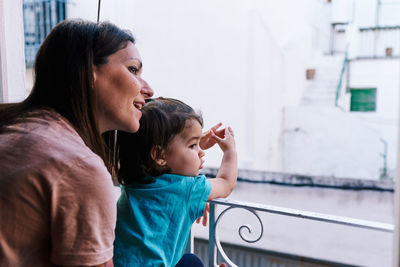 Mother and daughter looking out the window of the house happy