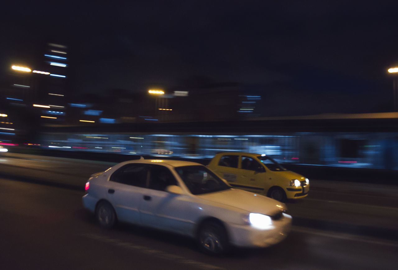 CARS MOVING ON ROAD IN CITY AT NIGHT