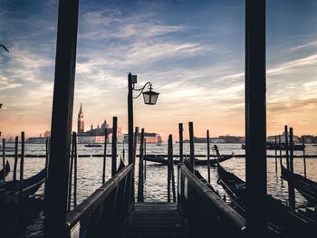 Wooden posts in sea against cloudy sky