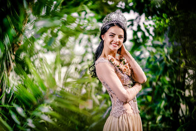 Portrait of beautiful bride wearing crown while standing amidst plants at botanical garden