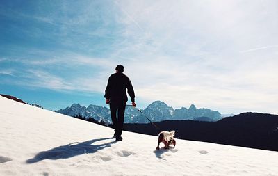 Rear view of man with dog on snow covered mountain against sky