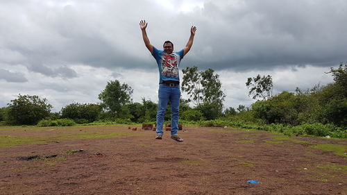 Happy man jumping on field against cloudy sky