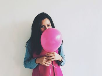 Portrait of young woman with pink balloons against white background