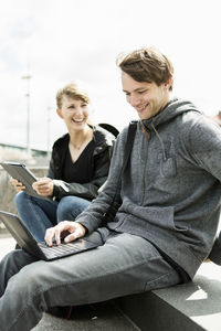 Happy young college friends using laptops on campus