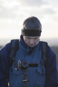 Mature man using camcorder while standing against sky