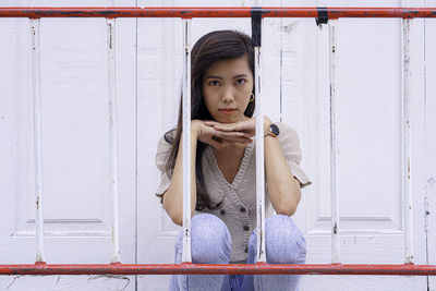 Portrait of beautiful young woman sitting against wall