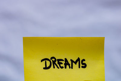 Close-up of yellow sign on wall against sky