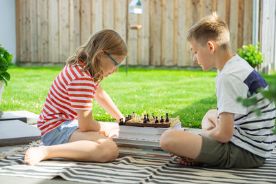 Rear view of boy playing with boys sitting outdoors