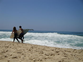 Rear view of surfers walking on the beach