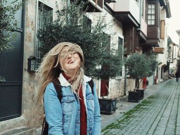 Young woman tossing hair while standing against building in city