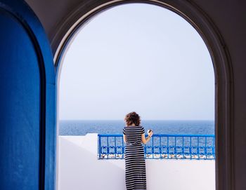 Rear view of woman with coffee cup standing in balcony against clear sky