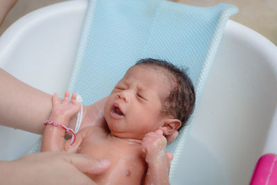 Cropped hands of woman holding baby boy in bathtub