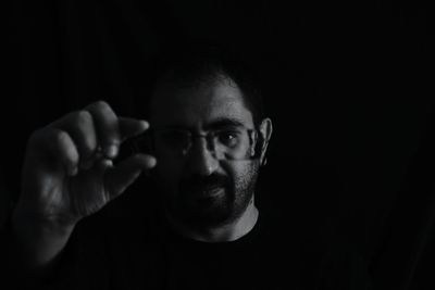 Close-up portrait of man holding eyeglasses in darkroom