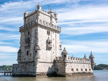 View of building by river against cloudy sky